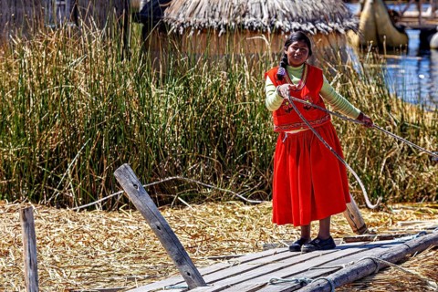 Woman in traditional dress rides a wooden reed boat in a lake, The floating reed islands of Uros in