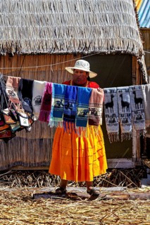 Woman showing colorful, handmade cloths in front of a thatched hut, The floating reed islands of