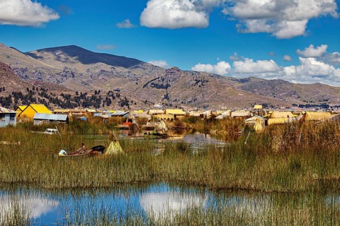 A rural area with huts, reeds and boats against a mountain backdrop and blue skies, The floating