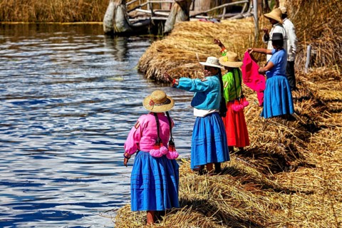 Women in colorful traditional clothing stand on the shore and look out at the water, the floating