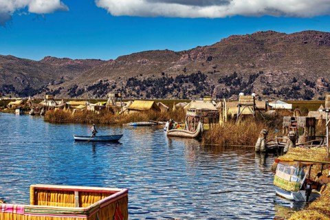 Canoe on a lake with traditionally built reed huts and mountains, The floating reed islands of the