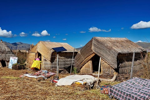 Reed huts with solar panels under a clear blue lakeside sky, The floating reed islands of the Uros