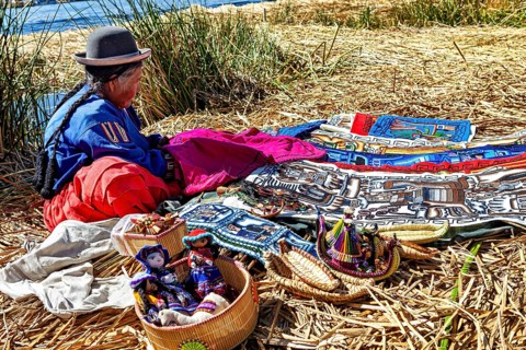 Woman sitting at colorful crafts on an island near a lake, The floating reed islands of Uros in