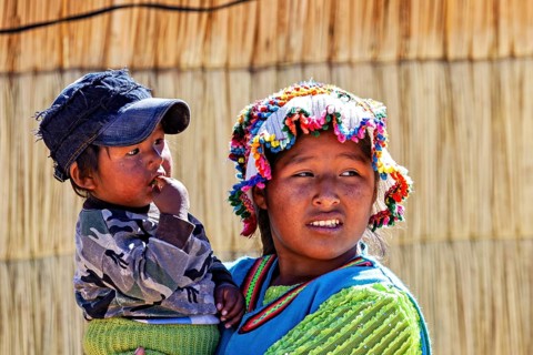 Woman wearing colorful hat carrying a child in her arms, both in traditional clothing, The floating