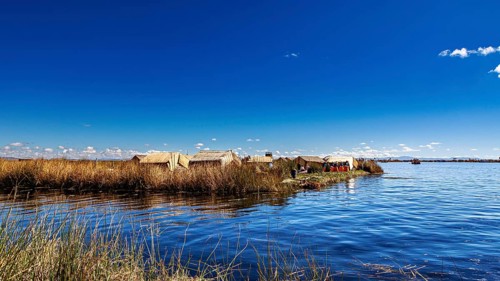 View of reed huts on the coast of a lake under expansive blue sky, The floating reed islands of the