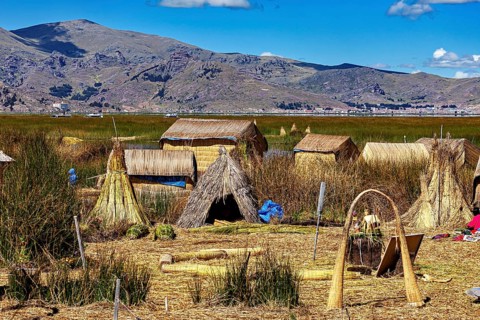 Traditional reed huts on the edge of a lake with mountains in the background, The floating reed