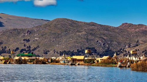Huts on the shores of a lake in front of a mountainous landscape under a blue sky, The floating