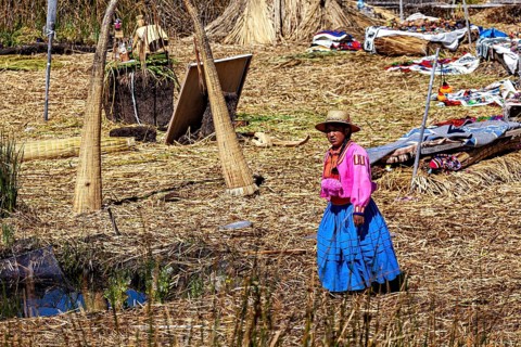 A woman in traditional dress stands in a quiet village made of reeds, The floating reed islands of