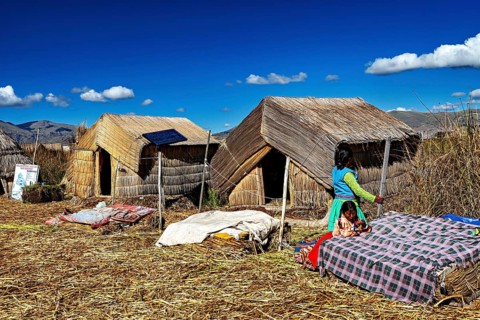 Woman approaches huts made of reeds, dressed in traditional clothing, The floating reed islands of