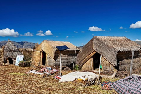 Traditional reed huts with solar panels on a lake surrounded by mountains, The floating reed