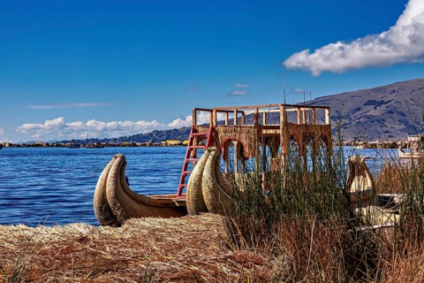 A traditional reed boat is lying on the shores of the lake under a cloudy sky, The floating reed