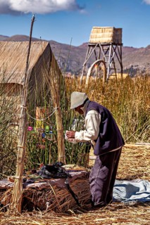 Man is engaged in handicraft work next to traditional reed huts, the floating reed islands of the