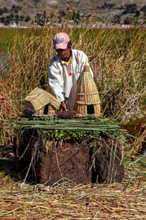 Man showing a model of straw huts and figures on a natural surface, The floating reed islands of