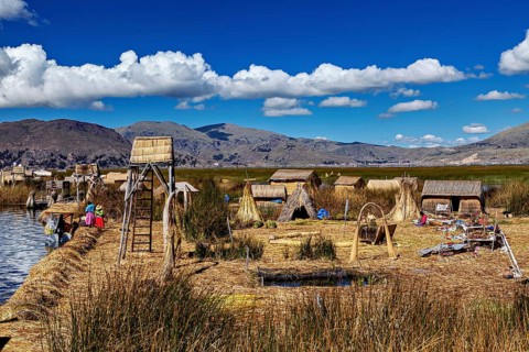 A traditional village with reed huts and views of mountains under cloudy skies, The floating reed