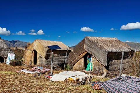 Several reed huts with solar panels under a blue lakeside sky, The floating reed islands of the