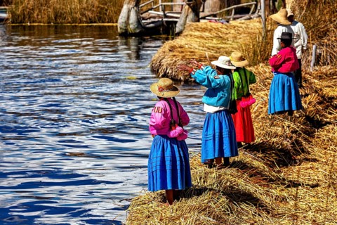 A group of woman in colorful, traditional clothing on the watery shore, The floating reed islands
