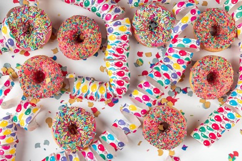 Donuts with colorful icing surrounded by confetti and streamers on a white background, carnival