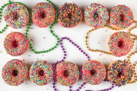 Donuts with colorful icing and sprinkles surrounded by colored pearl necklaces on a white