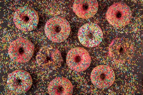 Donuts with sprinkles on wooden table, colorful ornaments scattered