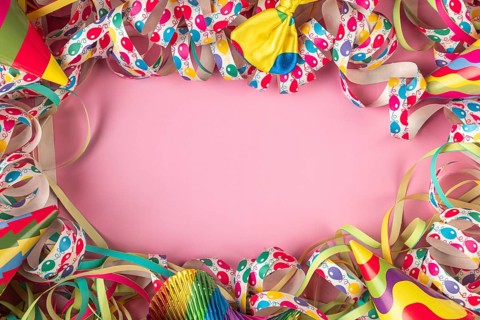 Party hats and colorful streamers frame a pink background, Mardi Gras