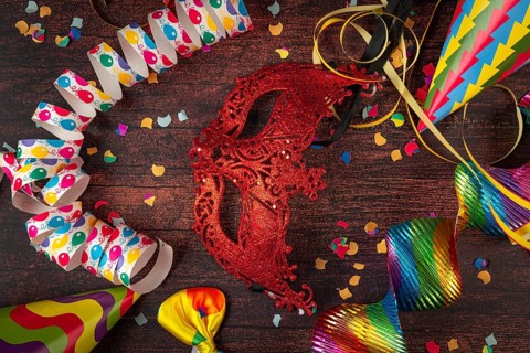 Red mask surrounded by party decorations such as streamers and confetti on table, carnival