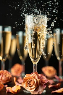 Sparkling wine made of glass surrounded by other glasses and rose petals on a black background