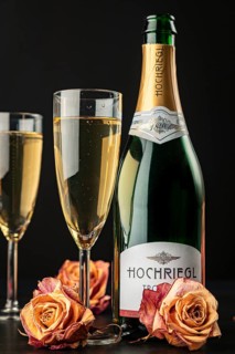 Champagne bottle and glasses decorated with dry roses on dark background