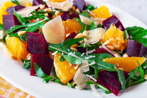 A salad made with chunks of beet, orange slices, and arugula. It is topped with cheese shavings and