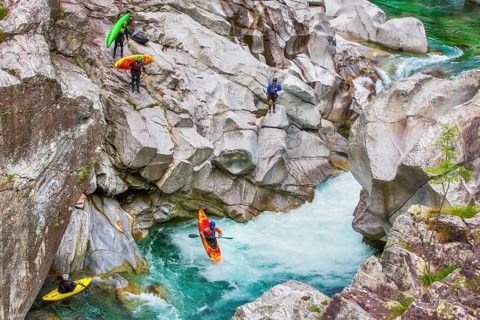 Group of tourists canyoning with canoes, jumping from the rocks of the Verzasca River in summer,