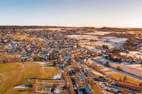 An aerial perspective of a sprawling village with snow-covered fields and settlements under clear