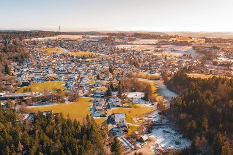 A village surrounded by forest and hills, with snow-covered areas and a river in winter,