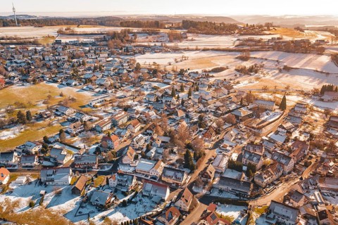 Wide settlement in winter with snow-covered roofs and fields in sunlight from an aerial