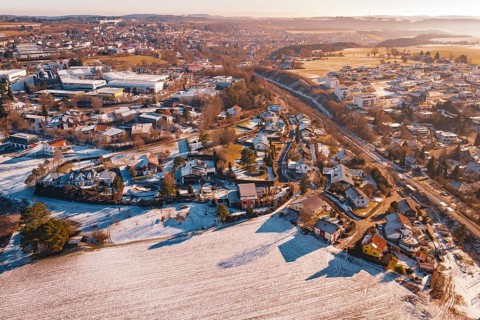 Aerial view of a rural village, partly covered by snow, with roads and trees under clear sky,