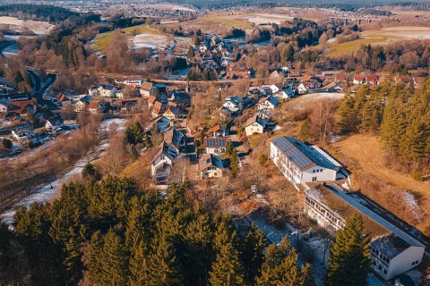 Panoramic view of a village with snow-covered roofs surrounded by forest and hills, Aach,