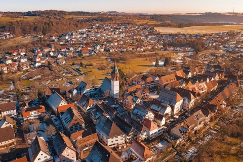 Aerial view of a town with church and buildings in evening light, surrounded by hills and fields,