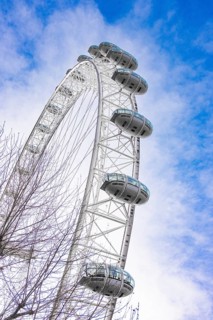 A large Ferris wheel juts into the blue sky surrounded by clouds, London Eye, London, United
