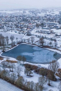 Snowy village with frozen lake seen from above on a grey day, Empfingen, Freudenstadt district,