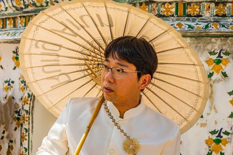Young man wearing a parasol in traditional clothing presents himself for the photographers, Wat