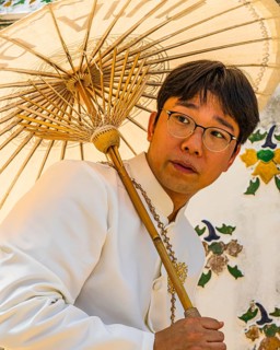 Young man wearing a parasol in traditional clothing presents himself for the photographers, Wat