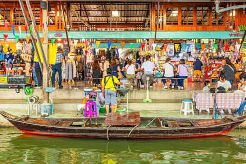 Wooden boat on the Damneon Saduak floating markets channel, behind shops and restaurant, near