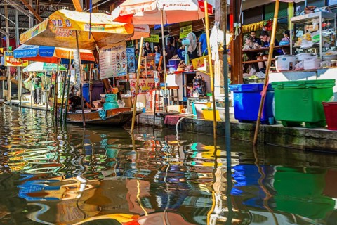 Wooden boat and umbrellas are reflected on the Damneon Saduak floating market channel near Bangkok,