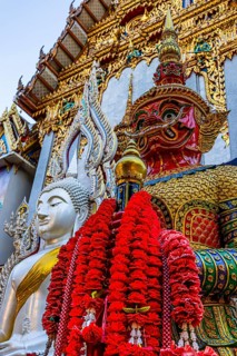Richly decorated Buddha statue at Wat Suthiwararam Buddhist temple, guarded by a yaksha, Bangkok,