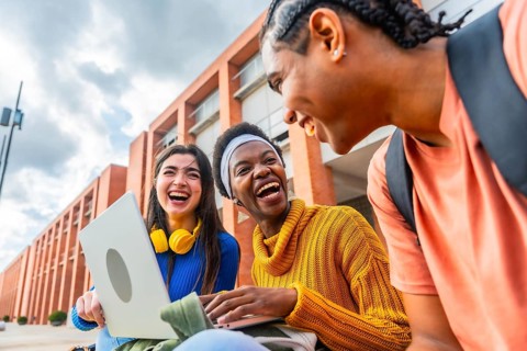 Three young, diverse students are happily laughing and sharing a lighthearted moment while