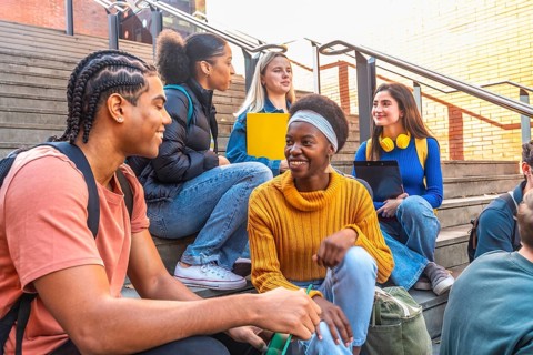 Diverse group of young students sitting on university campus steps, happy and smiling while