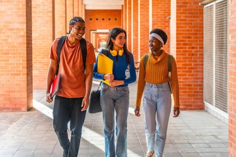 Diverse students walking through a university building on campus, carrying backpacks and notepads,