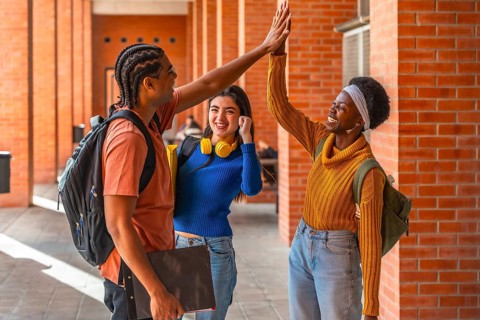 Diverse university students high fiving outdoors, celebrating teamwork and friendship on campus,
