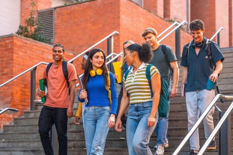 Diverse group of smiling university students walking down outdoor stairs on campus together,