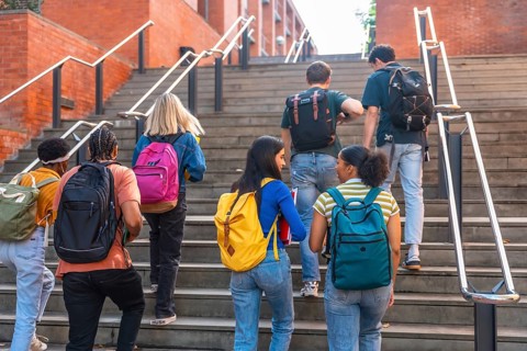 Group of young, multi ethnic university students with backpacks ascending outdoor stairs at a
