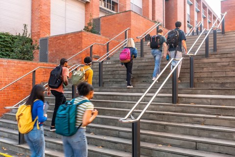 Diverse group of university students climbing outdoor campus stairs with backpacks, heading toward