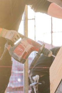 Close-up of workers with drill, wood and sunlight on construction site, carpentry construction,